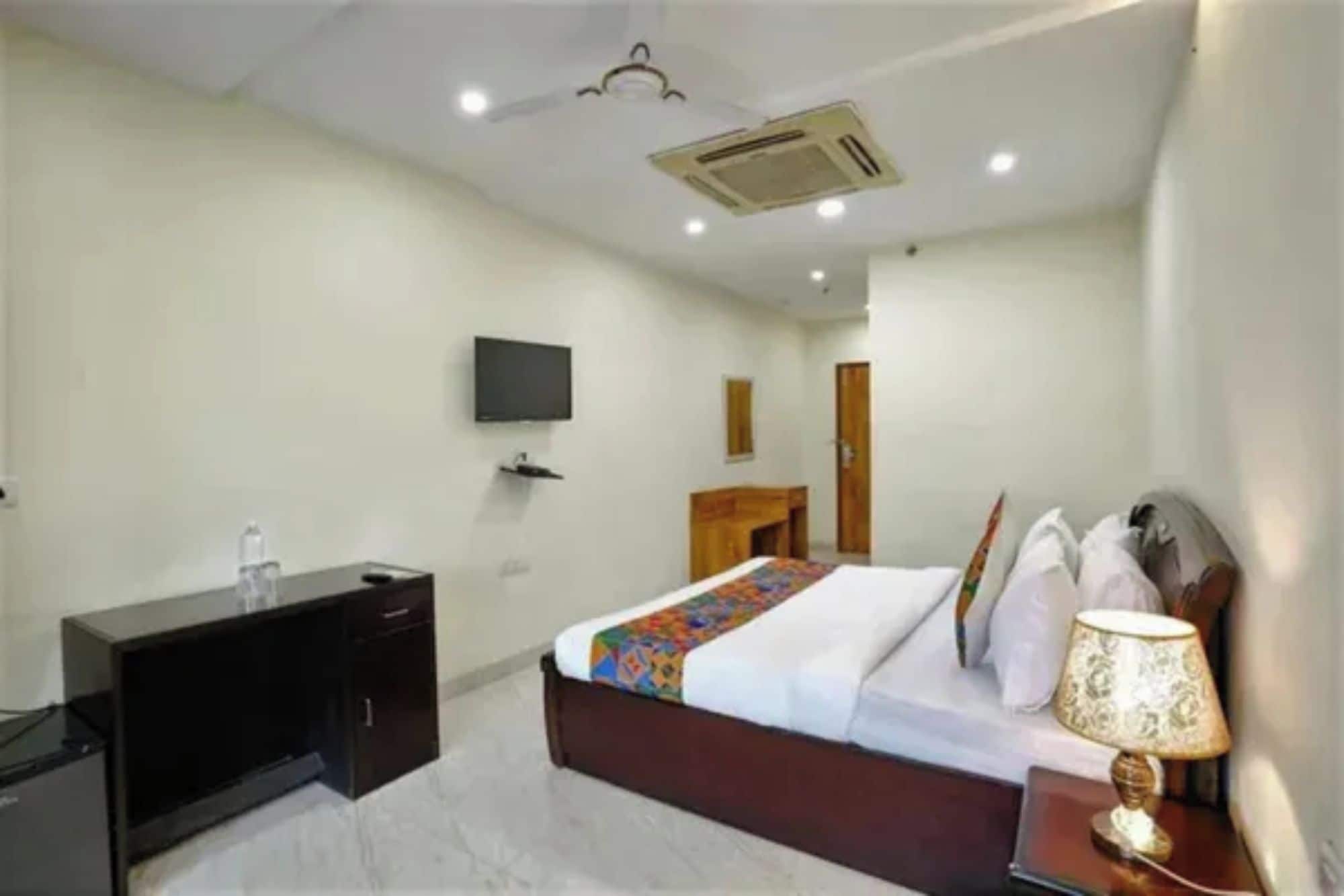 A hotel room with a bed, bedside table, lamp, TV, wardrobe, and a desk.