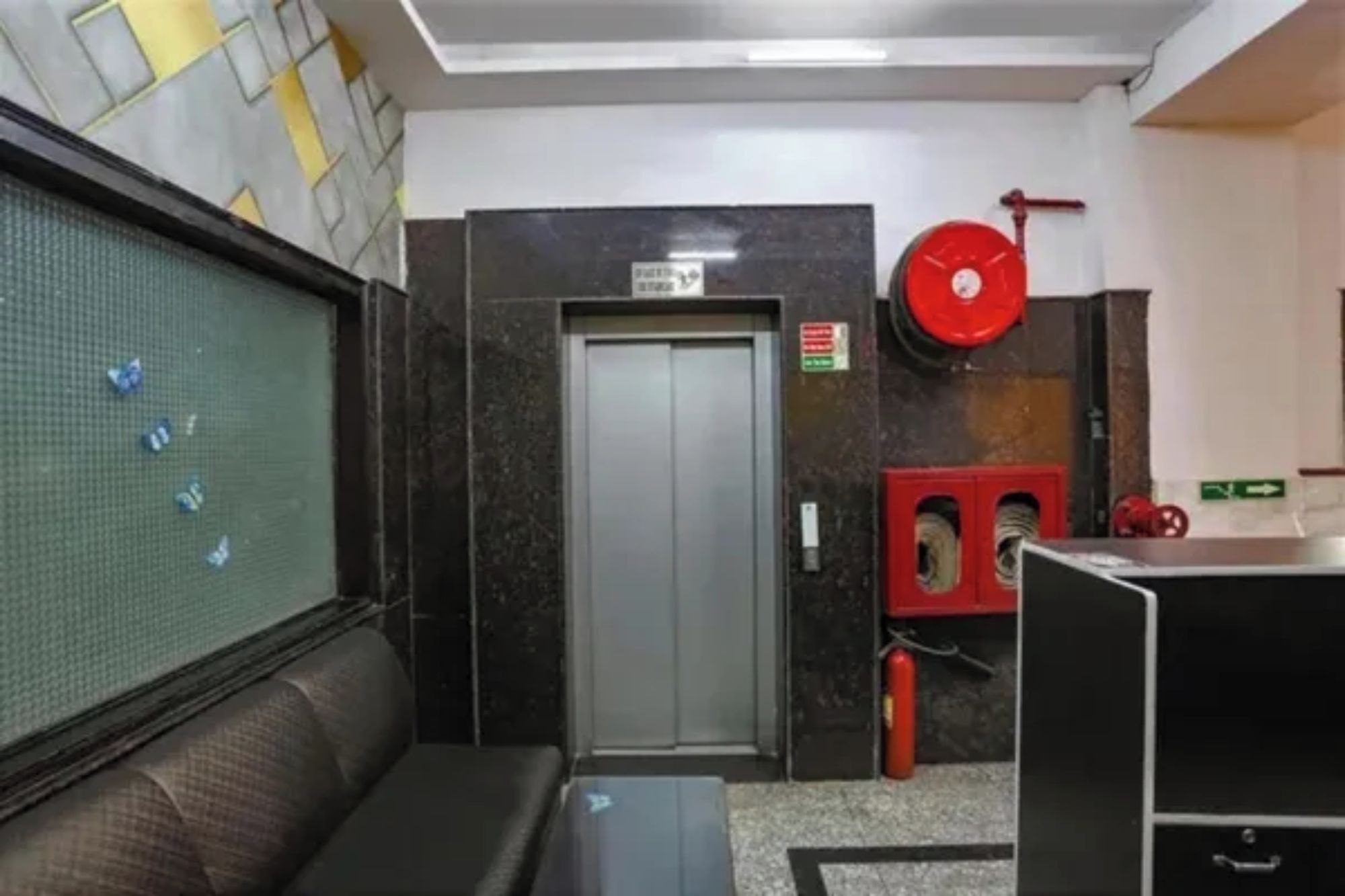 Un hall de hotel con una recepción, un sofá, una puerta y un extintor rojo.