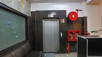 Un hall de hotel con una recepción, un sofá, una puerta y un extintor rojo.