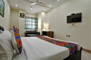 Una habitación de hotel con una cama, un televisor montado en la pared y un escritorio con una lámpara.