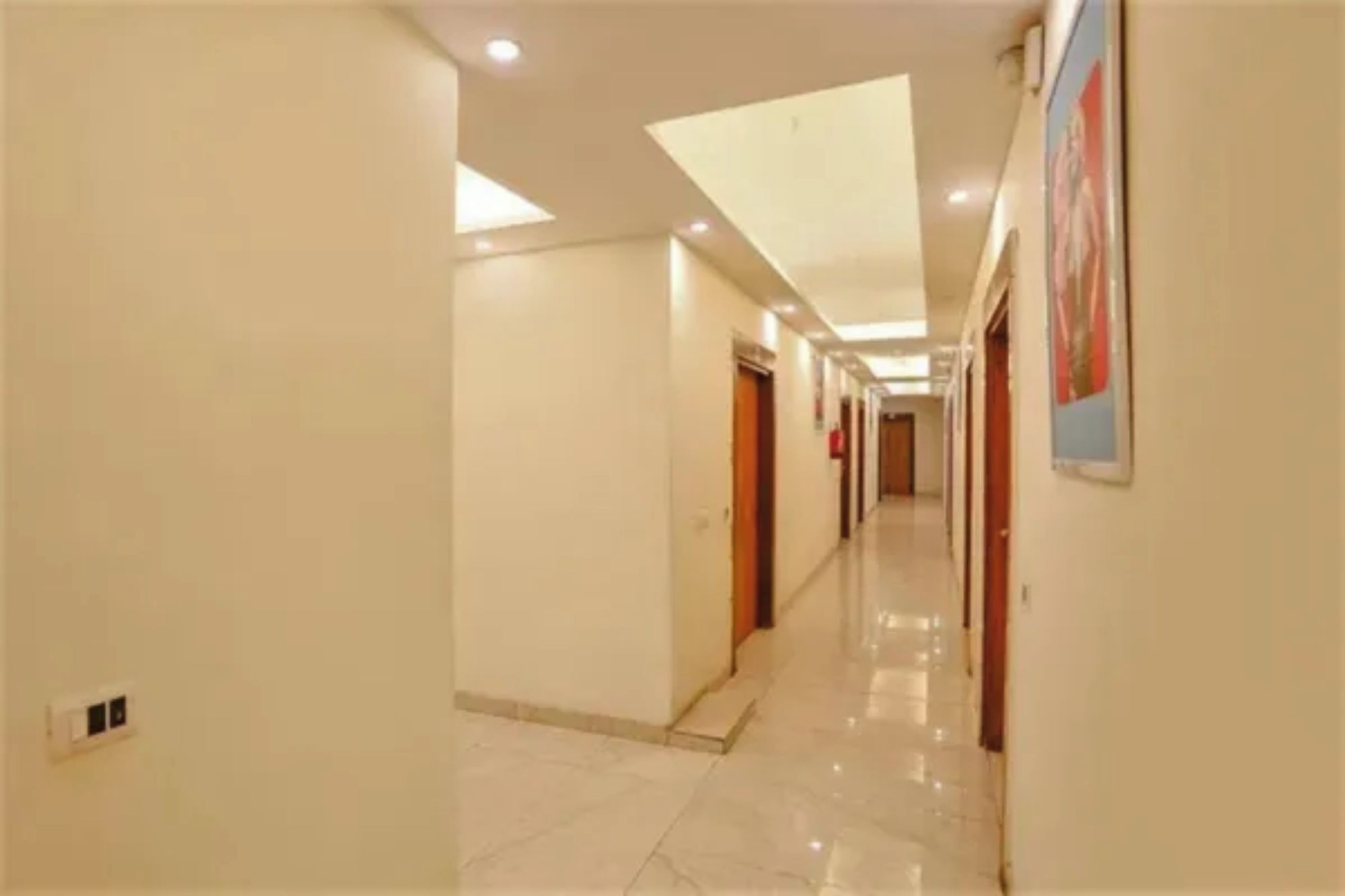 Un pasillo de hotel con puertas a ambos lados, suelo de baldosas e iluminación empotrada en el techo.