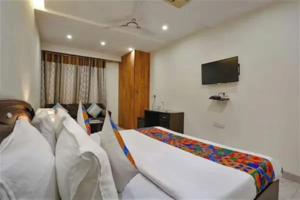 Habitación de hotel con cama, escritorio, silla, televisor montado en la pared y ventana con cortinas.