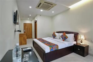 Una habitación de hotel con cama, mesita de noche, lámpara y vista al pasillo.