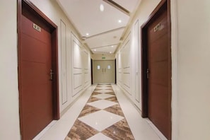 A hotel corridor with a checkered floor pattern, double doors on either side, and a ceiling with recessed lighting. - FabHotel Amazing Stays - Vikaspuri (New Delhi)