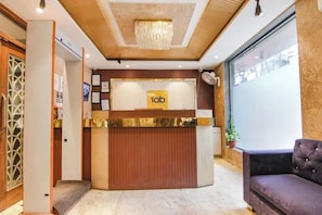 A hotel reception desk with a chandelier, a plush sofa, and framed certificates on the wall. - FabHotel Amazing Stays - Vikaspuri (New Delhi)