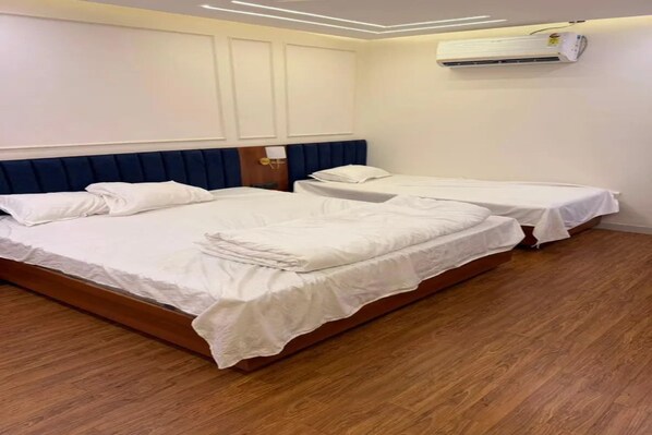 Habitación de hotel con dos camas, suelo de madera y un equipo de aire acondicionado en la pared.