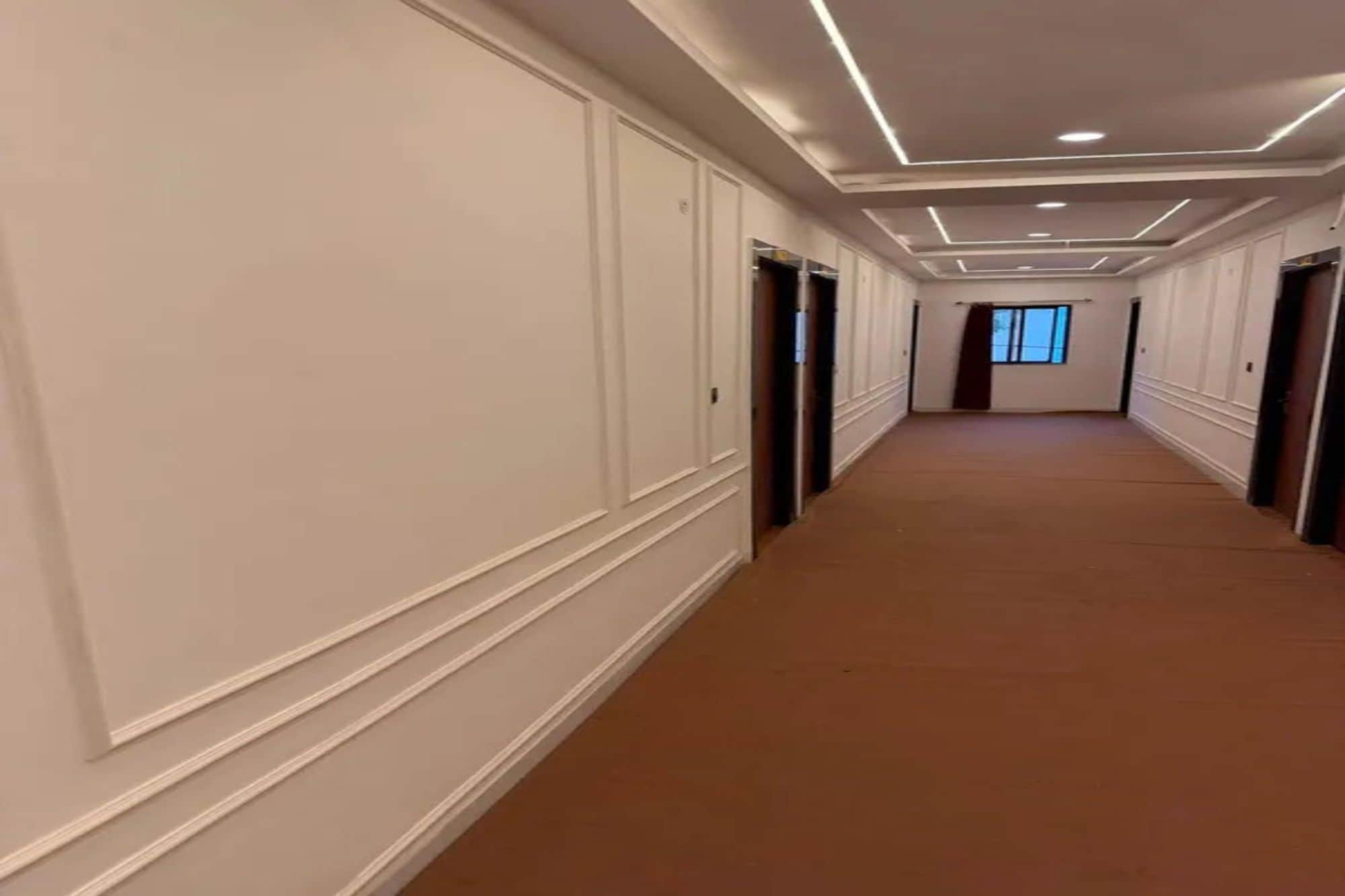 Un largo y estrecho pasillo con puertas a ambos lados, que conduce a una habitación con ventana.