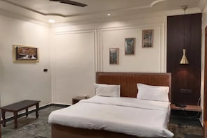 A hotel room with a bed, a nightstand, a small table, and a wall-mounted lamp. - FabHotel Amantran (Kanpur)