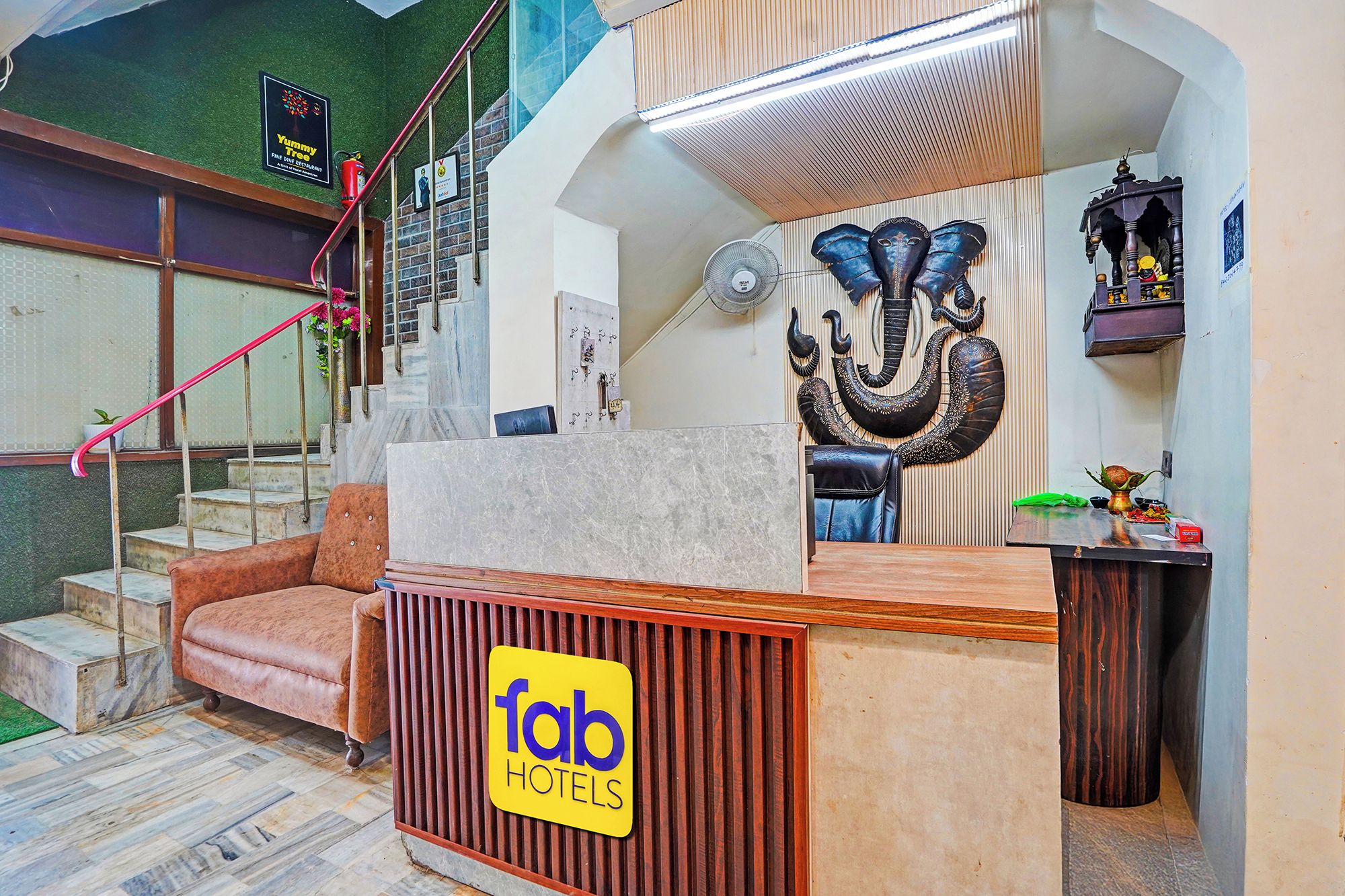 A hotel reception area with a marble counter, a staircase with a red handrail, and a wall-mounted sculpture.
