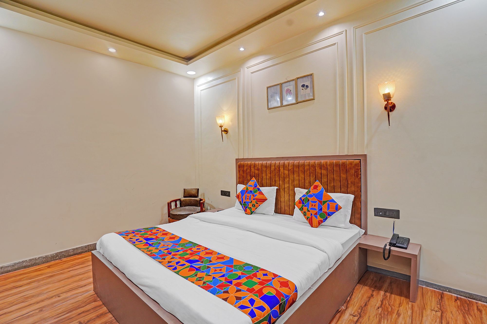 A hotel room with a large bed, a wooden headboard, a bedside table with a phone, and wall-mounted lights.