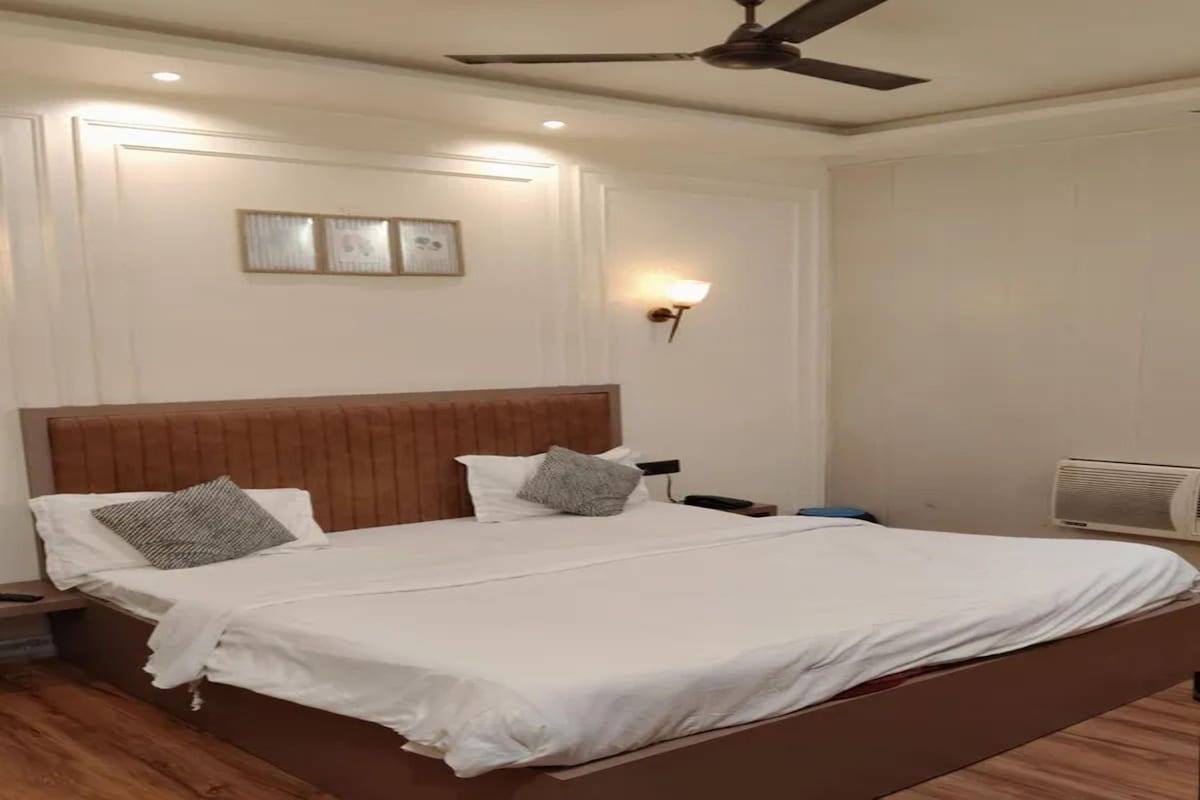 A double bed with a wooden headboard, a bedside table, a wall-mounted lamp, and a ceiling fan.