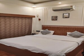 A hotel room with a large bed, a wooden headboard, an air conditioning unit, and a wall-mounted lamp. - FabHotel Amantran (Kanpur)