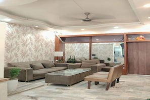 A modern living room with a sectional sofa, a glass coffee table, and a wooden chair. - FabHotel Amantran (Kanpur)
