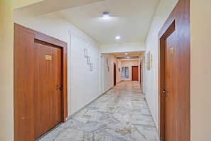 A hotel corridor with wooden doors, numbered room signs, and a tiled floor. - FabHotel Amantran (Kanpur)