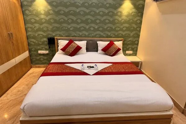Cama bem arrumada com colcha branca e vermelha, cabeceira de madeira e parede com padrão verde.