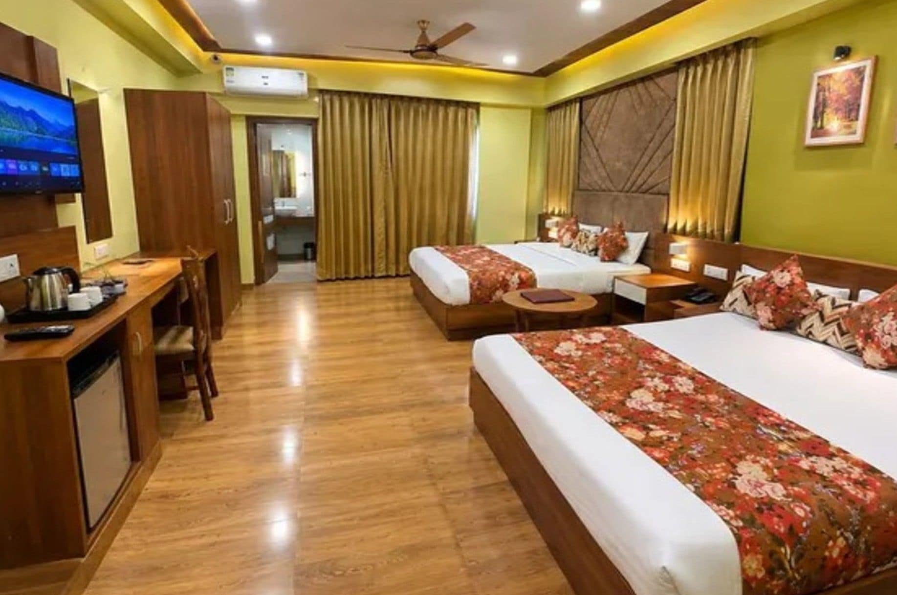 A hotel room with two beds, a desk, a television, and a ceiling fan.