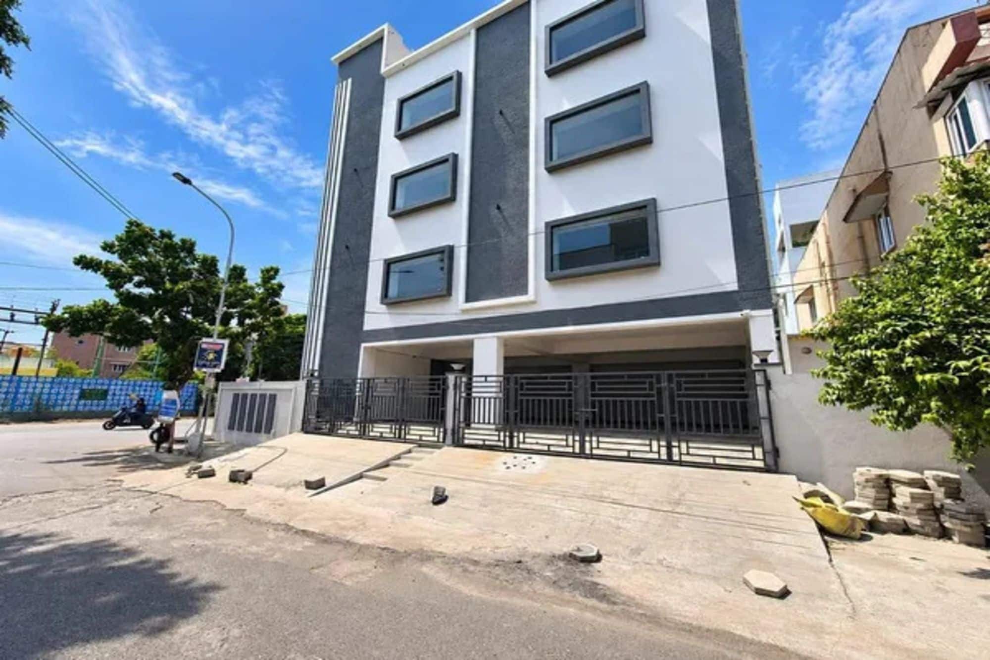 Un edificio de varios pisos con techo plano, entrada protegida por una reja y área pavimentada al frente.