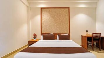 A hotel room with a large bed, a wooden headboard, a nightstand with a vase of flowers, and a desk with a chair.