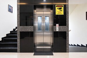 An elevator with a CCTV warning sign, a staircase with black steps, and a patterned wall.