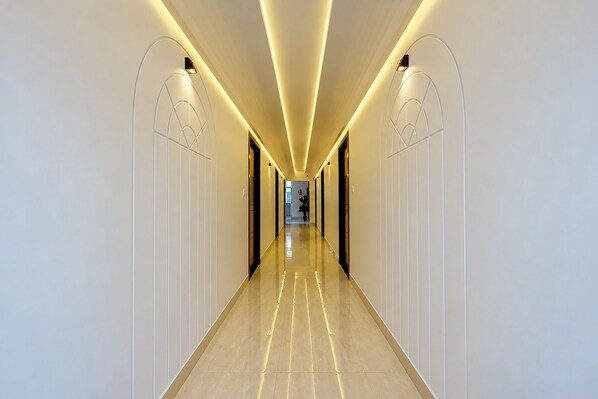 A modern hotel corridor with a long, straight path, light-colored walls, and a polished floor.