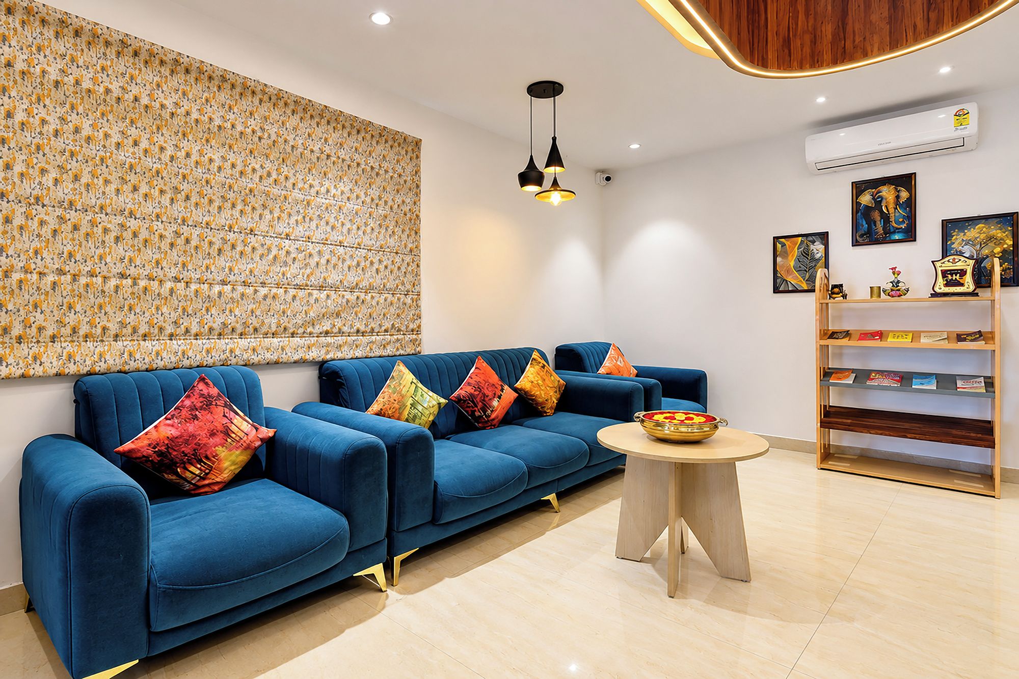 A modern living room with a blue sofa set, a round coffee table, and a bookshelf.
