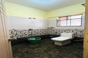 A bathroom with a toilet, a green bucket, and a window with bars. - FabHotel K Hotels (Bangalore)