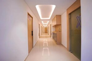 A modern hotel corridor with a long hallway, wooden doors, and a glass door with a logo. - FabHotel K Hotels (Bangalore)