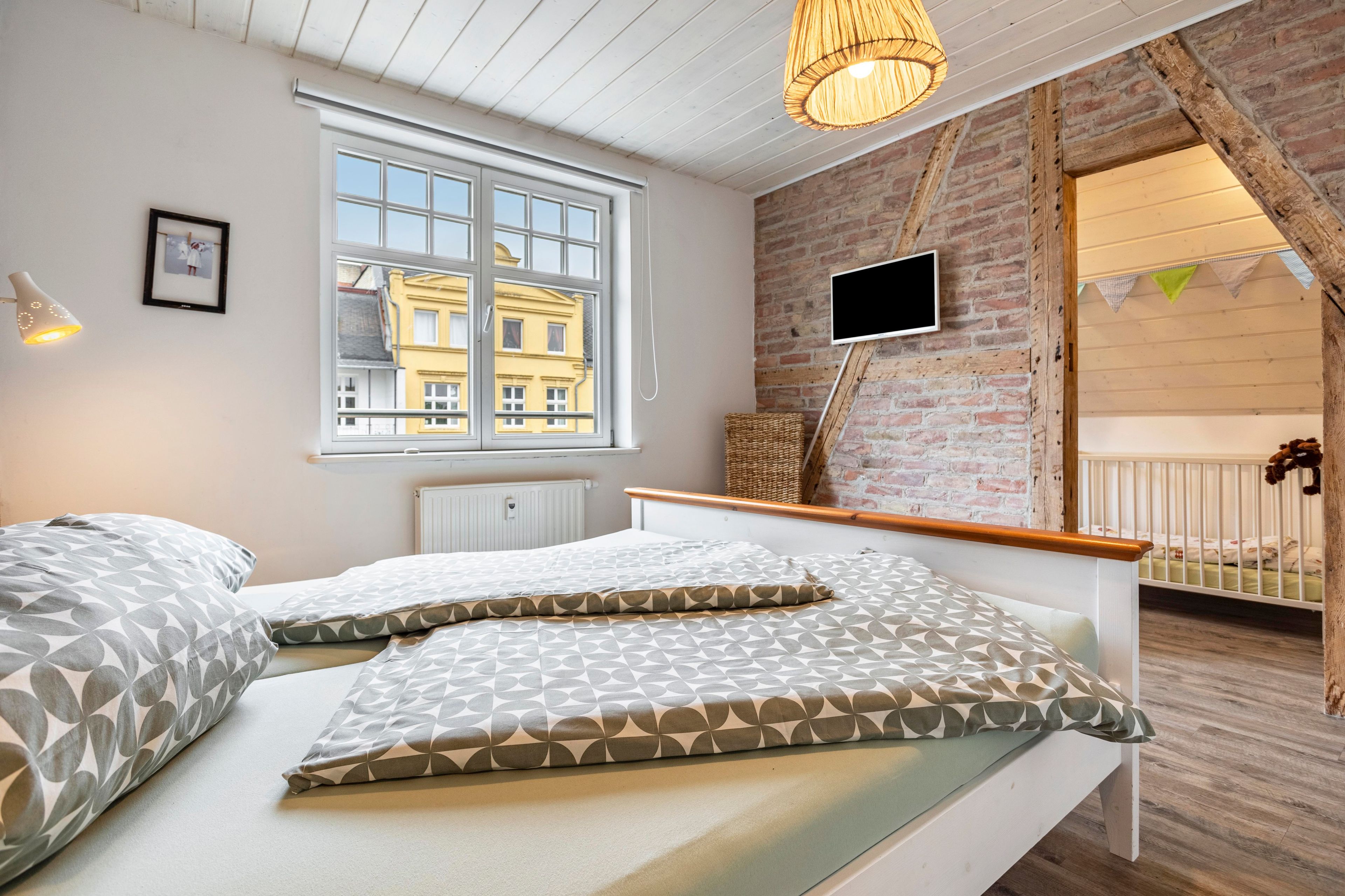 A bedroom with a bed, a window, a television, and a view of buildings outside.