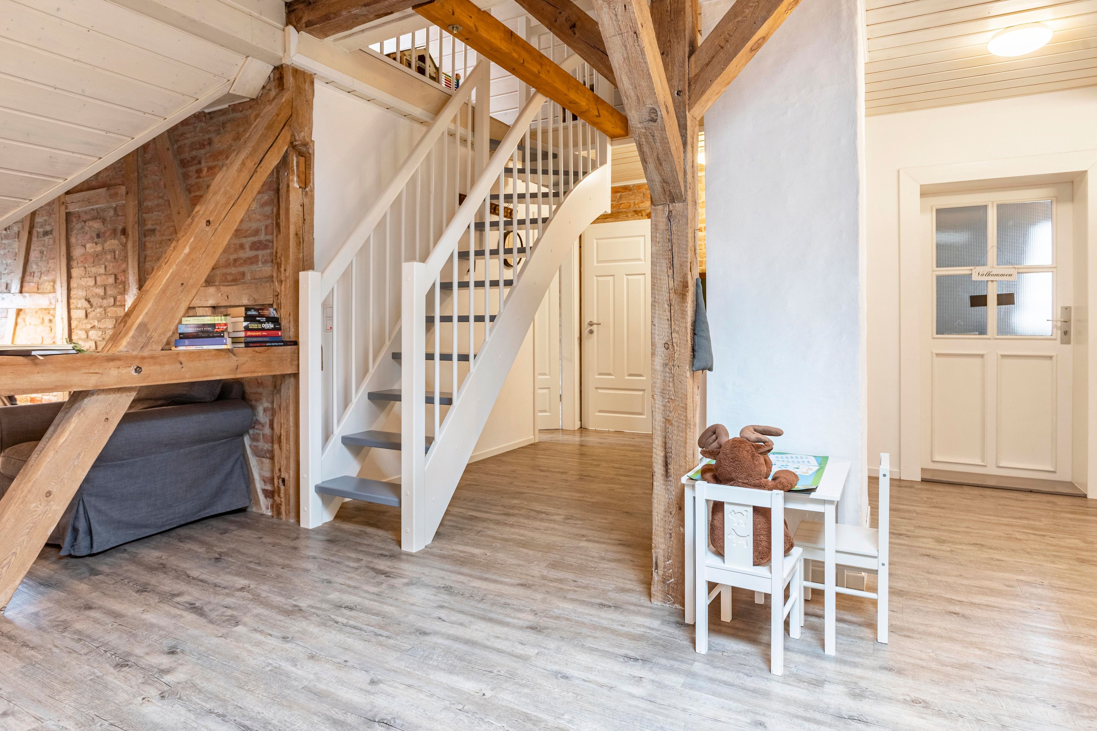 A room with a wooden staircase, a sofa, a table with a teddy bear, and a door with frosted glass panels.