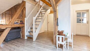 A room with a wooden staircase, a sofa, a table with a teddy bear, and a door with frosted glass panels.