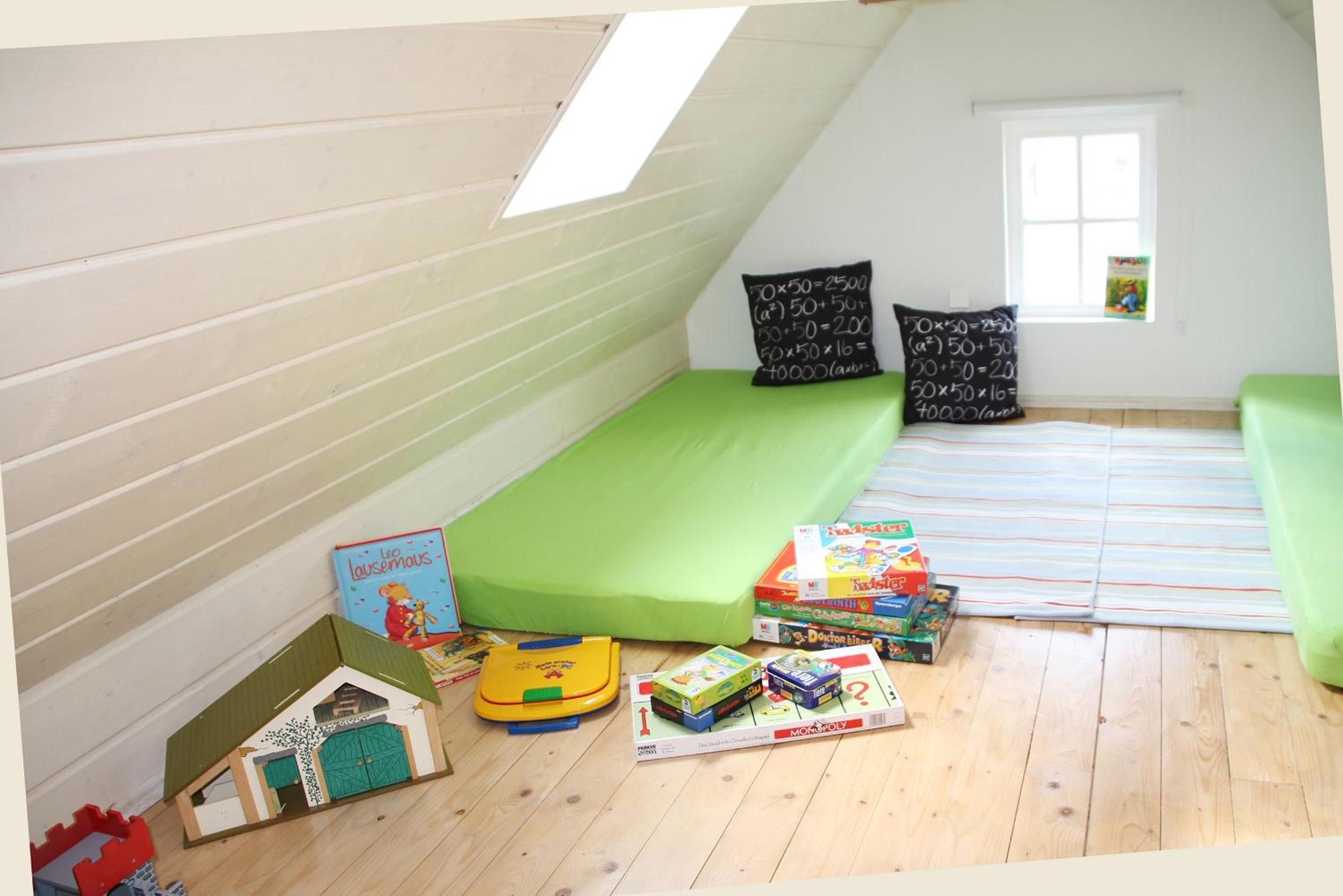 Una stanza giochi per bambini con un letto a soppalco, materasso verde e numerosi giocattoli e libri.