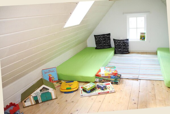 Una sala de jocs infantil amb un llit amb àtic, matalàs verd i diversos jocs i llibres.