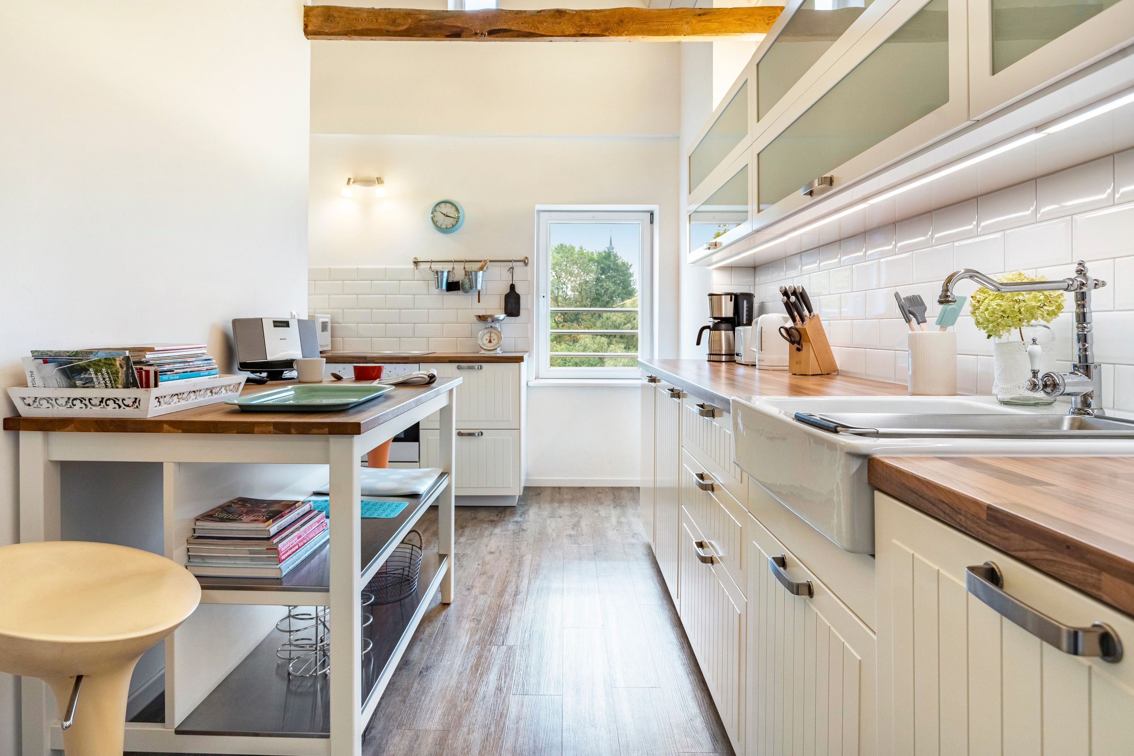 Eine moderne Küche mit weißen Schränken, einer Holz Arbeitsplatte und einem Fenster mit Blick auf Grünflächen.