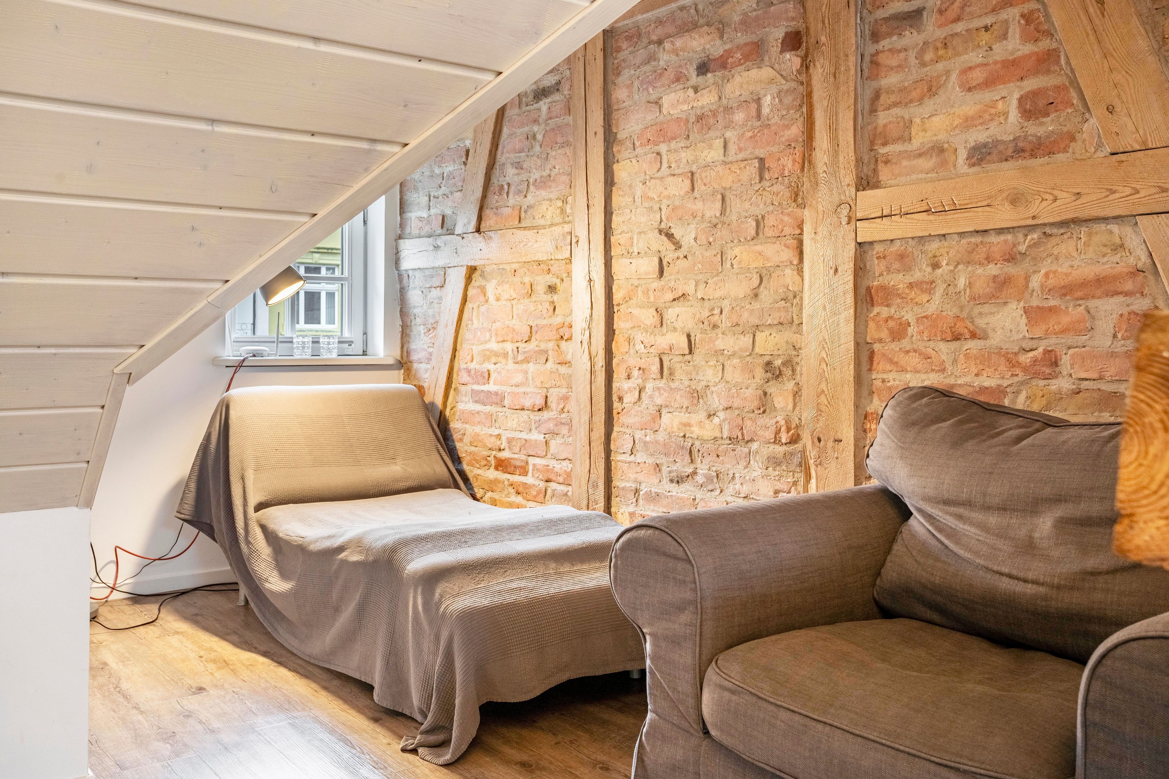 Ein Schlafzimmer im Loft-Stil mit freiliegenden Backsteinwänden, einer geneigten Decke und einem Fenster mit Blick auf eine Straße.