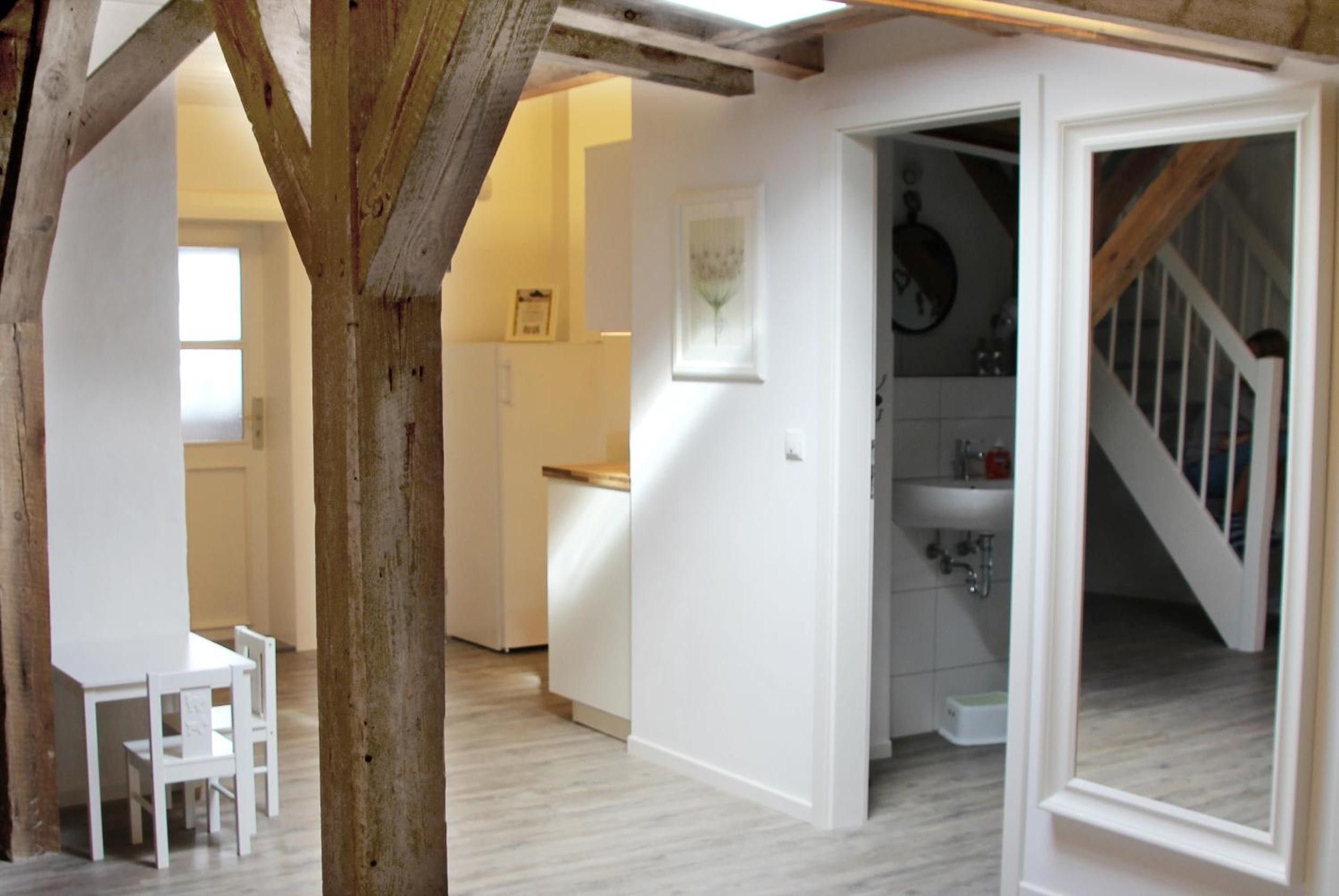 A room with a wooden beam ceiling, a white door leading to a bathroom, and a dining area with a table and chairs.
