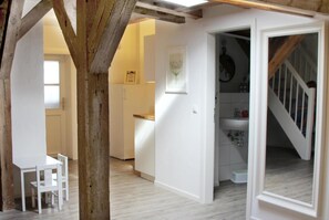 Una habitació amb sostre de bigues de fusta, una porta blanca que dona a un bany, i una zona de menjador amb taula i cadires.