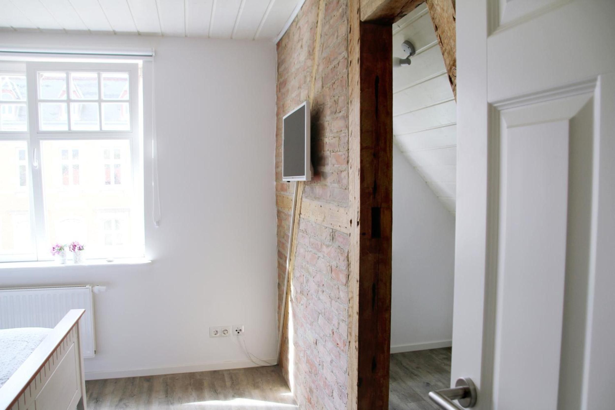 Une pièce avec un mur en briques, une fenêtre avec des stores, une porte et une prise électrique sur le mur.