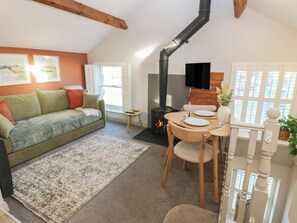 A cozy living room with a sofa, a dining table with chairs, a fireplace, and a television mounted on a wooden wall. - Dibble Cottage (Richmond)