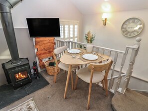 A cozy living room with a fireplace, a dining table set for two, and a television mounted on the wall. - Dibble Cottage (Richmond)
