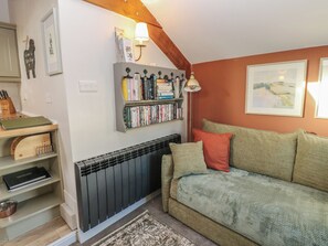 A cozy living room with a radiator, a bookshelf, a couch with cushions, and a framed painting on the wall. - Dibble Cottage (Richmond)