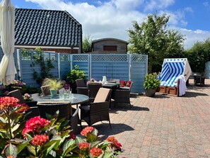 Ein möblierter Patio mit runden Tischen, Korbstühlen und einer überdachten Sitzgruppe.