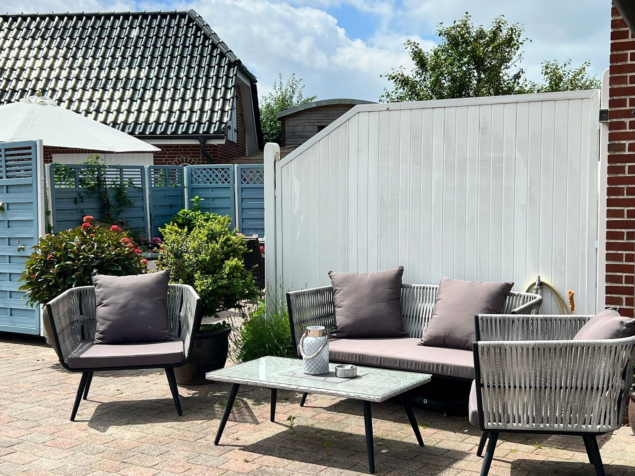 Une terrasse extérieure avec des meubles en osier, une table blanche et une clôture bleue.
