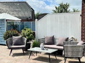 Une terrasse extérieure avec des meubles en osier, une table blanche et une clôture bleue.