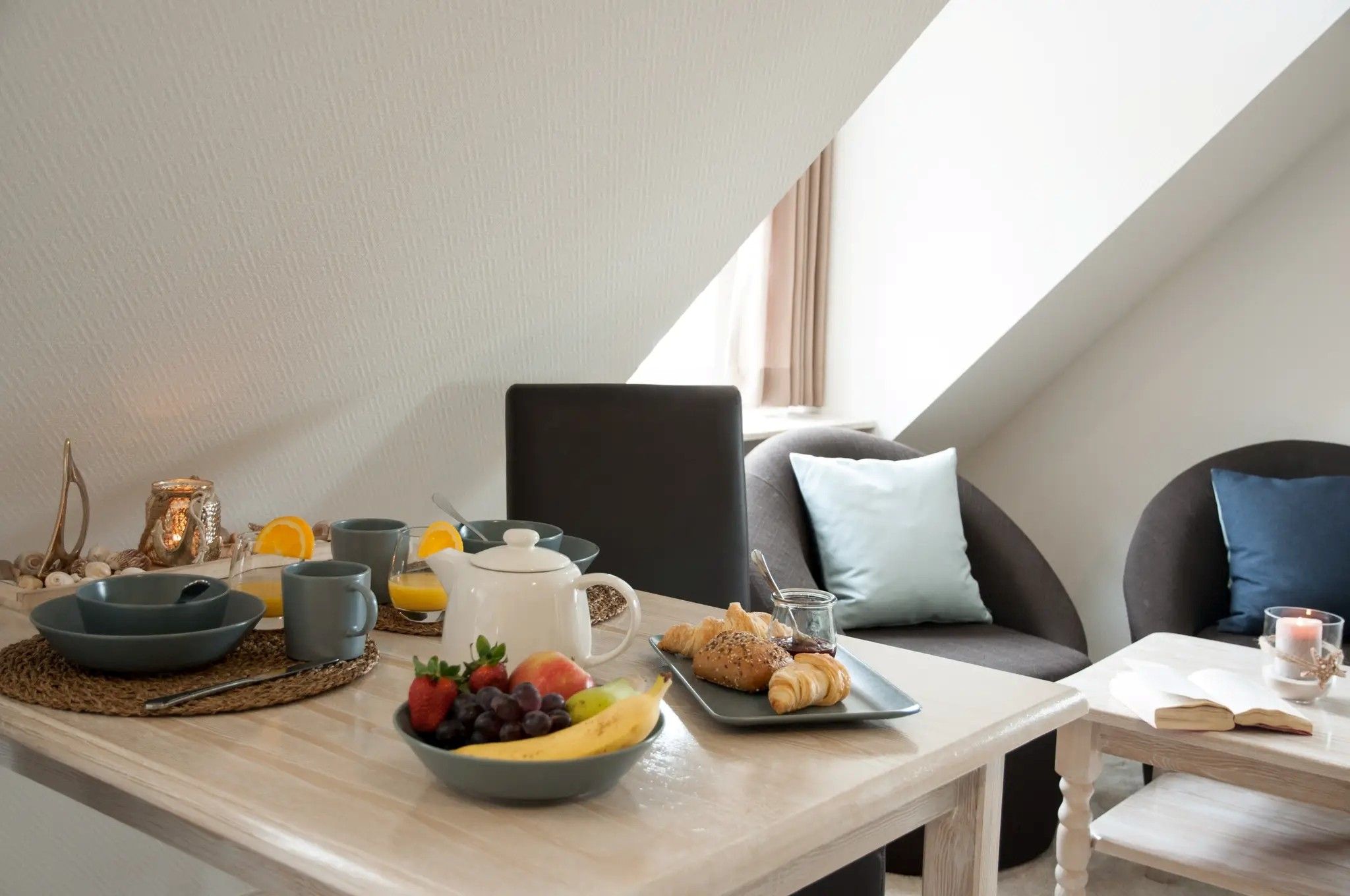 A breakfast setup with a bowl of fruit, croissants, and a coffee pot on a table.
