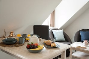 Une table dressée pour le petit-déjeuner, avec un saladier de fruits, des croissants et une cafetière.