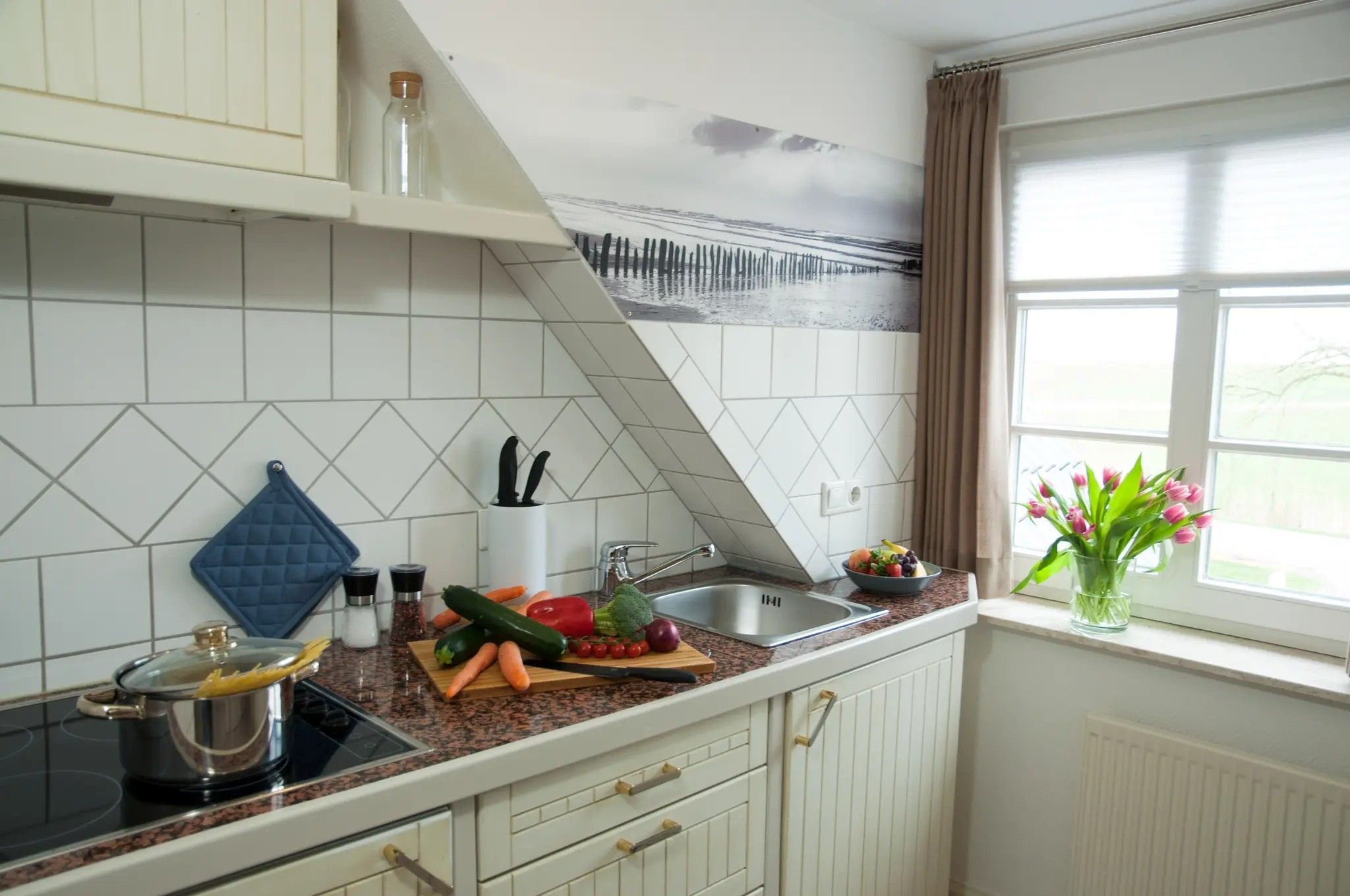 A kitchen with white cabinets, a granite countertop, a stove, a sink, and a window with curtains.
