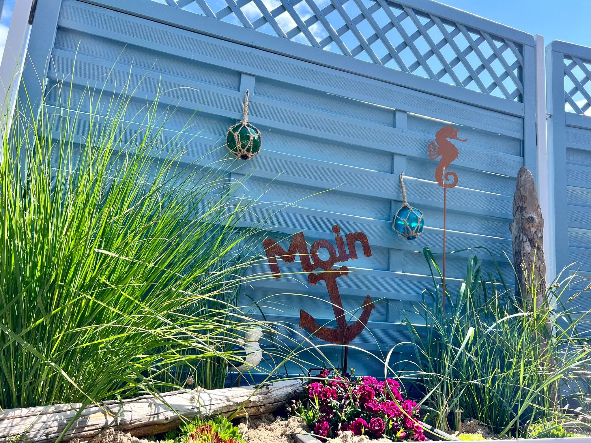 A building with a blue exterior, a wooden fence, and decorative elements including a seahorse and a hanging ornament.