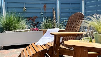 En udendørs siddeplads i træ med stol og bord, omgivet af planter og pynt.