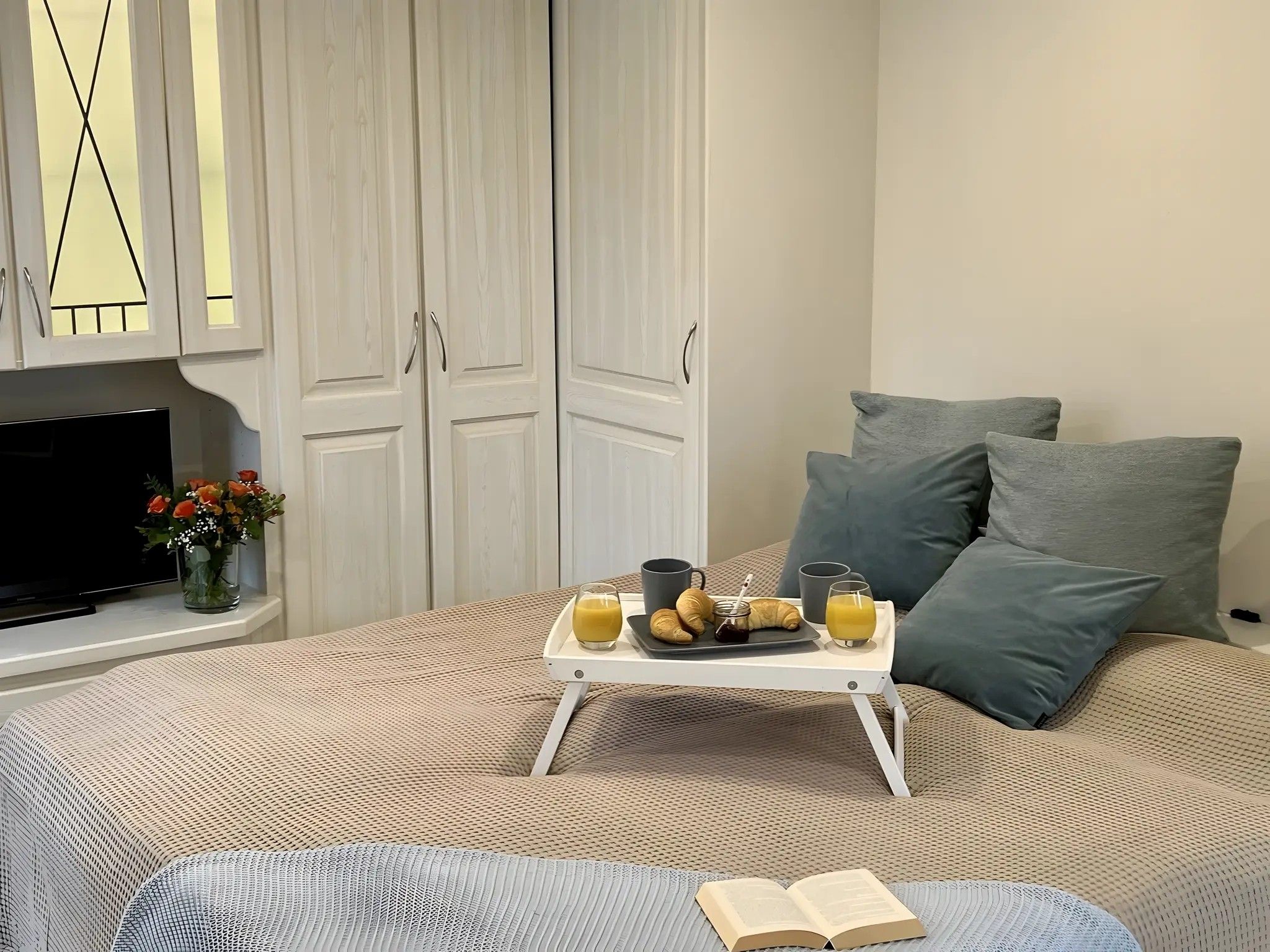 A bedroom with a bed, a bedside table with breakfast items, a TV, and a wardrobe.