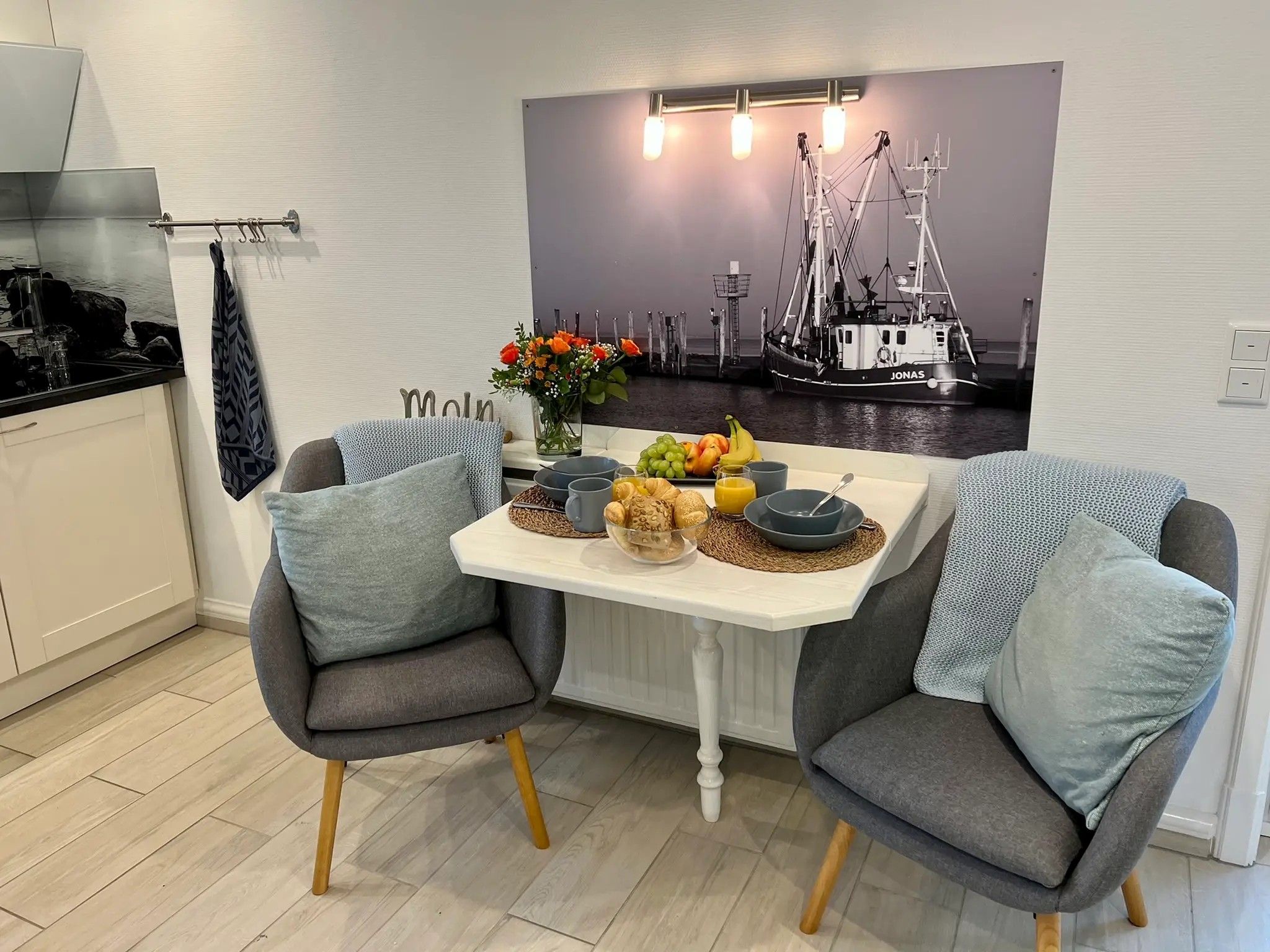 A dining area with a white table, two grey chairs, and a wall-mounted picture of a boat.